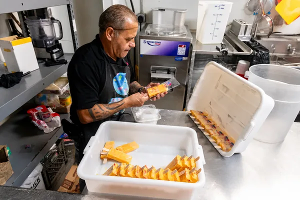 A staff member packaging paletas by hand in the kitchen.